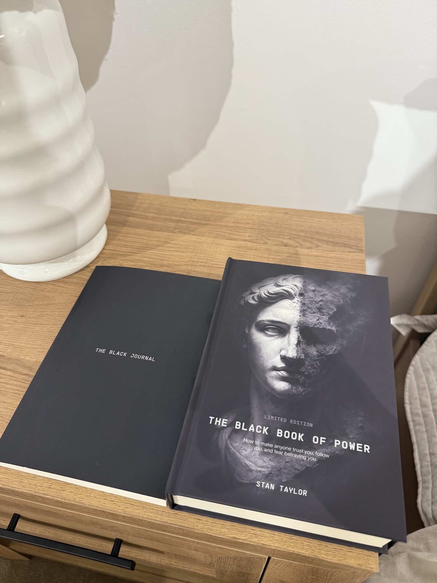 Two books titled 'The Black Journal' and 'The Black Book of Power' on a wooden surface.