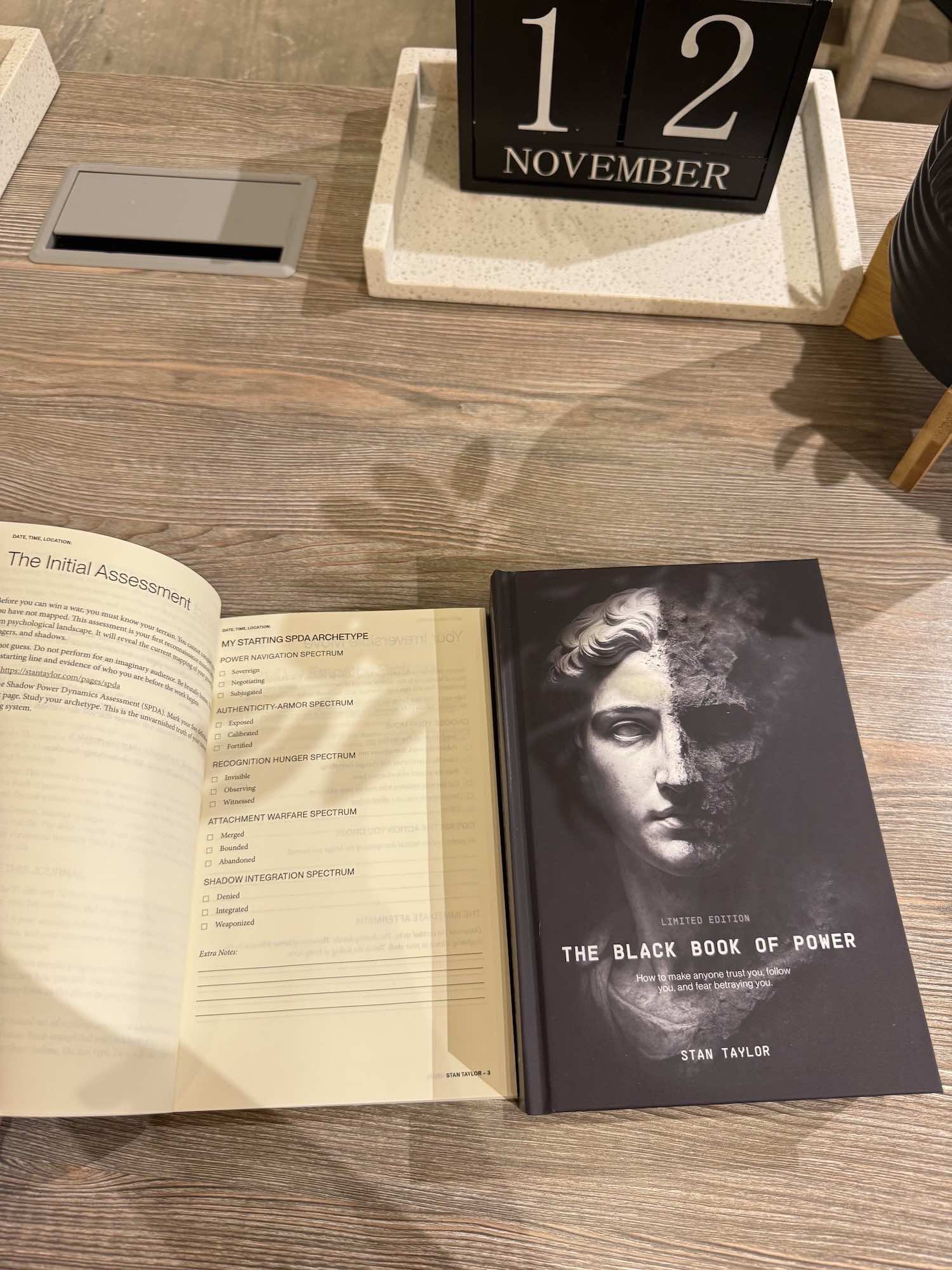 Open book and 'The Black Book of Power' on a wooden surface with a calendar showing November.