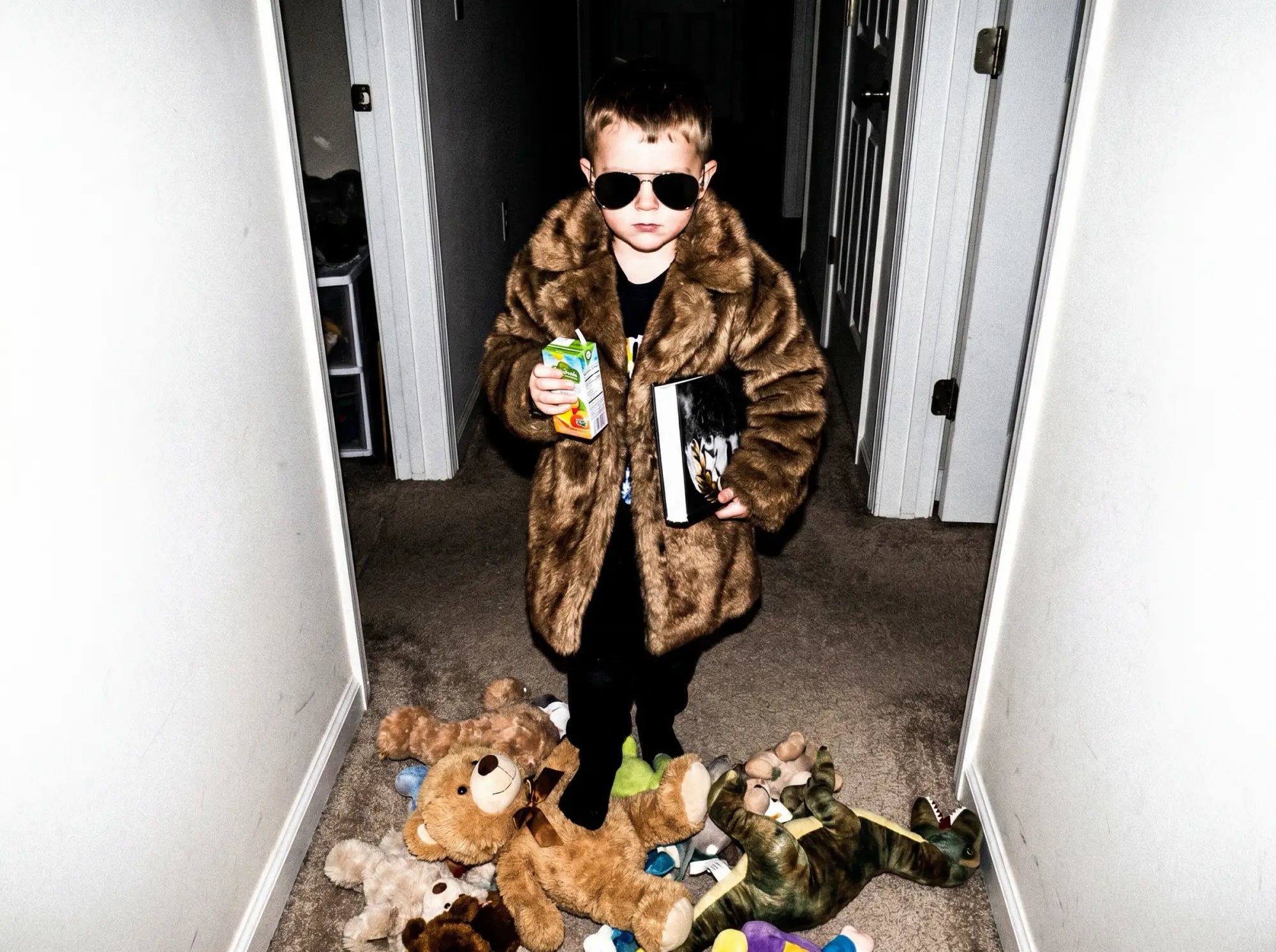 Child in fur coat and sunglasses amid scattered toys, drink in hand — The Little Dictator by Stan Taylor